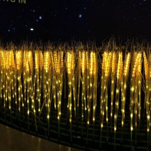 A dense row of illuminated golden wheat light sticks glowing brightly in the dark against a night sky background.