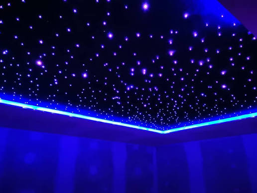 A custom-installed dark ceiling featuring vibrant blue fiber optic starlights, creating a realistic, glowing night sky effect within a modern interior space.